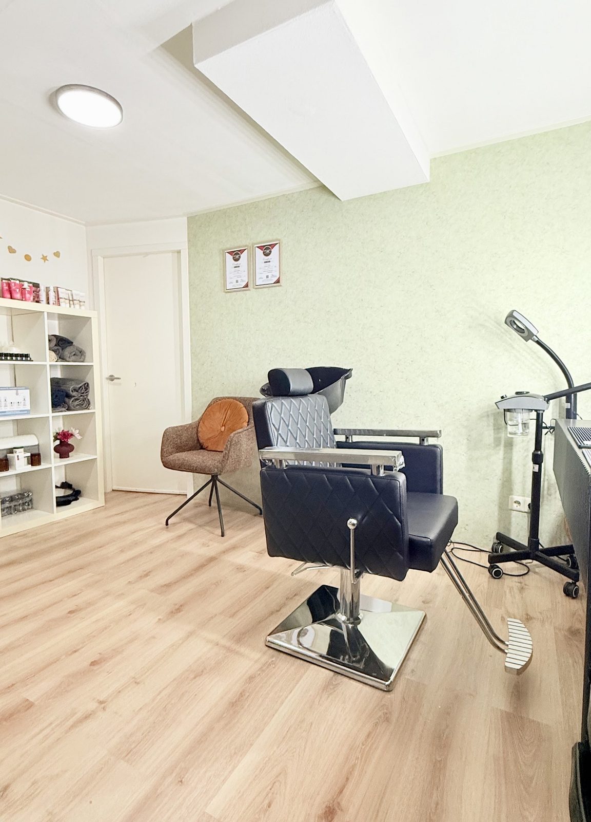 De salon met een kappersstoel, een behandellamp en een kast met producten